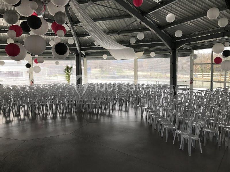 Salle décorée avec des lanternes suspendues, aménagée avec des rangées de chaises transparentes face à une ouverture vitrée.