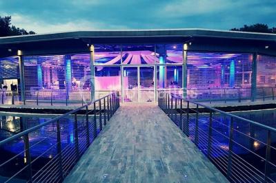 Kiosque en toit de chaume entouré d'arbres, situé dans une cour pavée avec des voiles d'ombrage.
