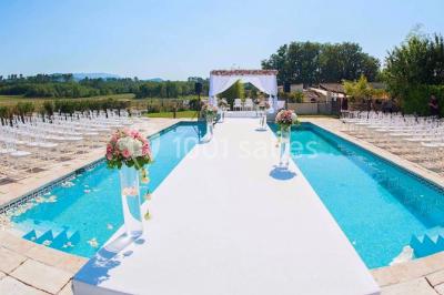 Kiosque en toit de chaume entouré d'arbres, situé dans une cour pavée avec des voiles d'ombrage.