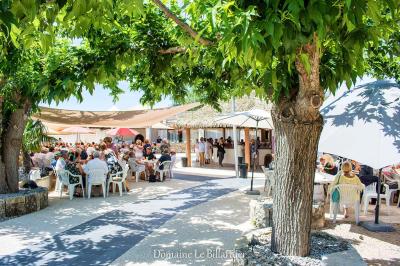 Kiosque en toit de chaume entouré d'arbres, situé dans une cour pavée avec des voiles d'ombrage.