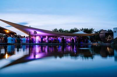 Kiosque en toit de chaume entouré d'arbres, situé dans une cour pavée avec des voiles d'ombrage.