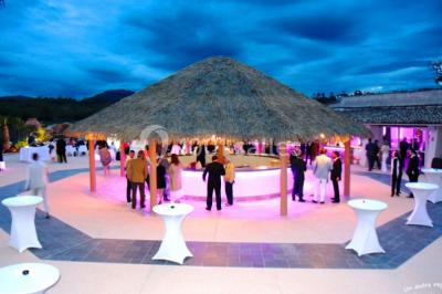 Kiosque en toit de chaume entouré d'arbres, situé dans une cour pavée avec des voiles d'ombrage.