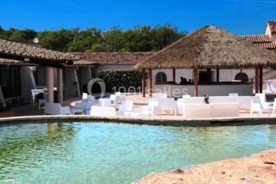 Kiosque en toit de chaume entouré d'arbres, situé dans une cour pavée avec des voiles d'ombrage.
