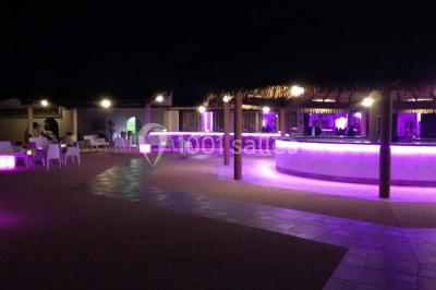 Kiosque en toit de chaume entouré d'arbres, situé dans une cour pavée avec des voiles d'ombrage.