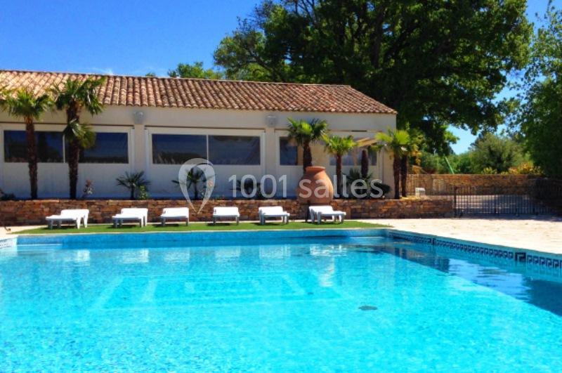 Piscine extérieure avec transats alignés devant un bâtiment à toit en tuiles, entourée de palmiers et végétation.