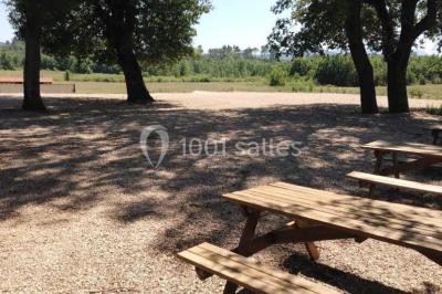 Kiosque en toit de chaume entouré d'arbres, situé dans une cour pavée avec des voiles d'ombrage.