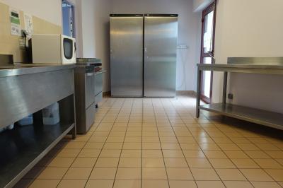 Salle de réception avec tables dressées, nappes blanches, chaises décorées et lumière naturelle entrant par les fenêtres.