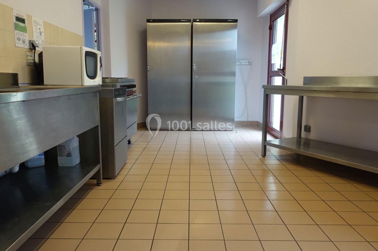 Cuisine professionnelle avec sol carrelé, plans de travail en inox, micro-ondes et deux grands réfrigérateurs en arrière…