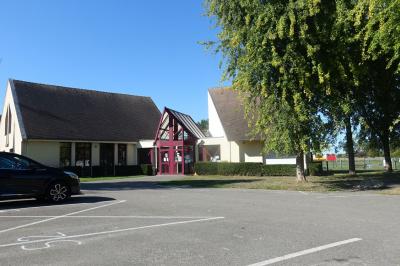 Salle de réception avec tables dressées, nappes blanches, chaises décorées et lumière naturelle entrant par les fenêtres.