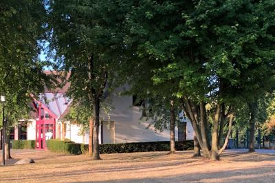 Salle de réception avec tables dressées, nappes blanches, chaises décorées et lumière naturelle entrant par les fenêtres.