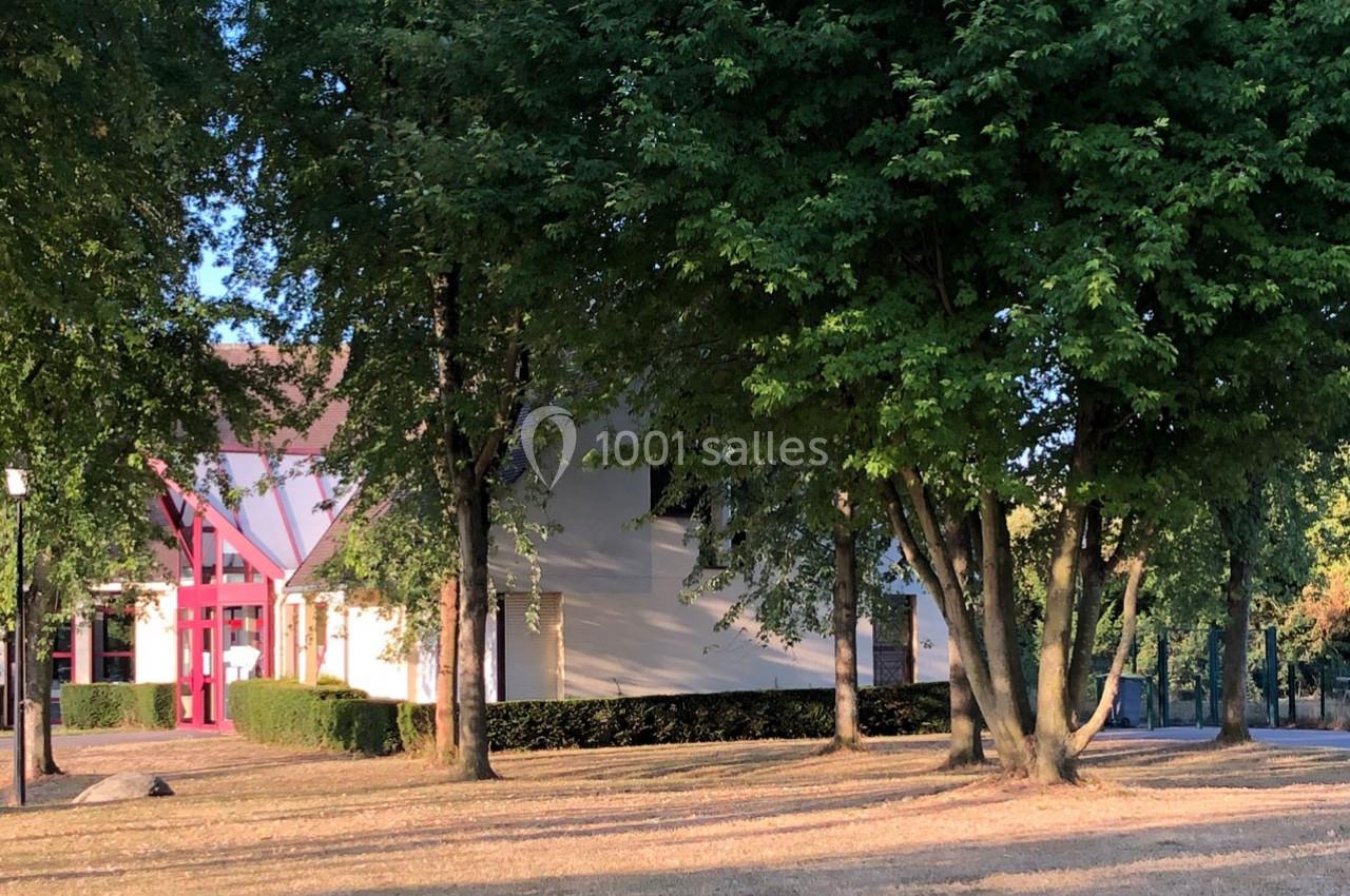 Bâtiment blanc avec façade rouge visible à travers des arbres dans un parc ensoleillé.