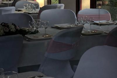 Salle de réception avec tables dressées, nappes blanches, chaises décorées et lumière naturelle entrant par les fenêtres.