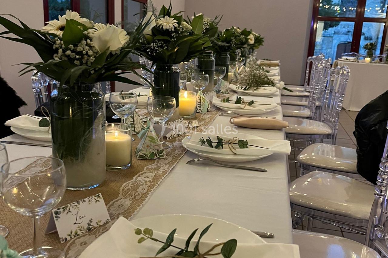 Table décorée pour un événement, avec nappes blanches, bouquets de fleurs, bougies et vaisselle élégante.