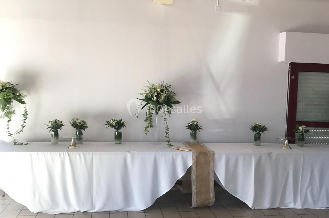Table décorée avec une nappe blanche, ornée de bouquets de fleurs vertes et blanches, dans une salle lumineuse.