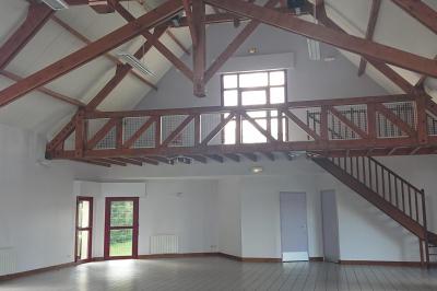 Salle de réception avec tables dressées, nappes blanches, chaises décorées et lumière naturelle entrant par les fenêtres.