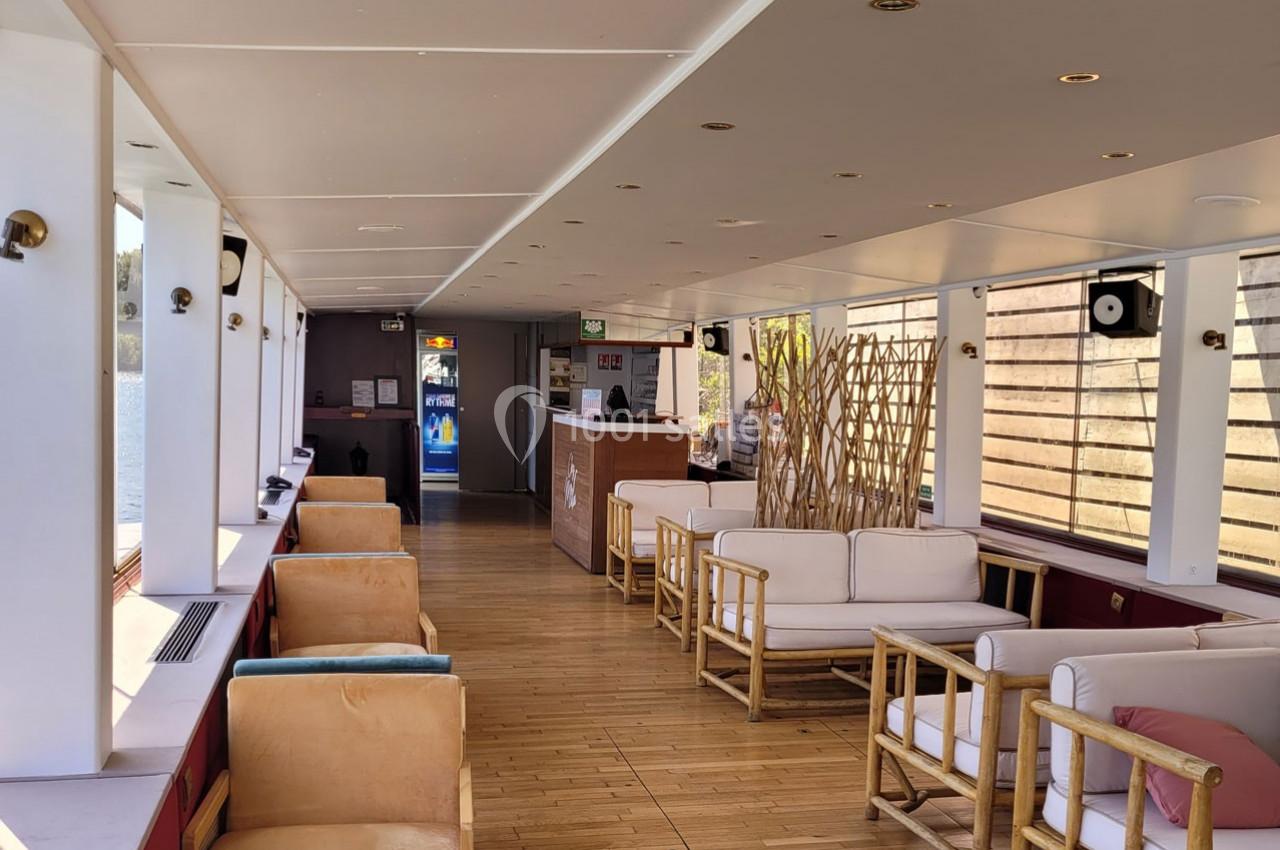 Intérieur lumineux d'un salon avec fauteuils en bois, canapés blancs et parquet, donnant sur un comptoir d'accueil.