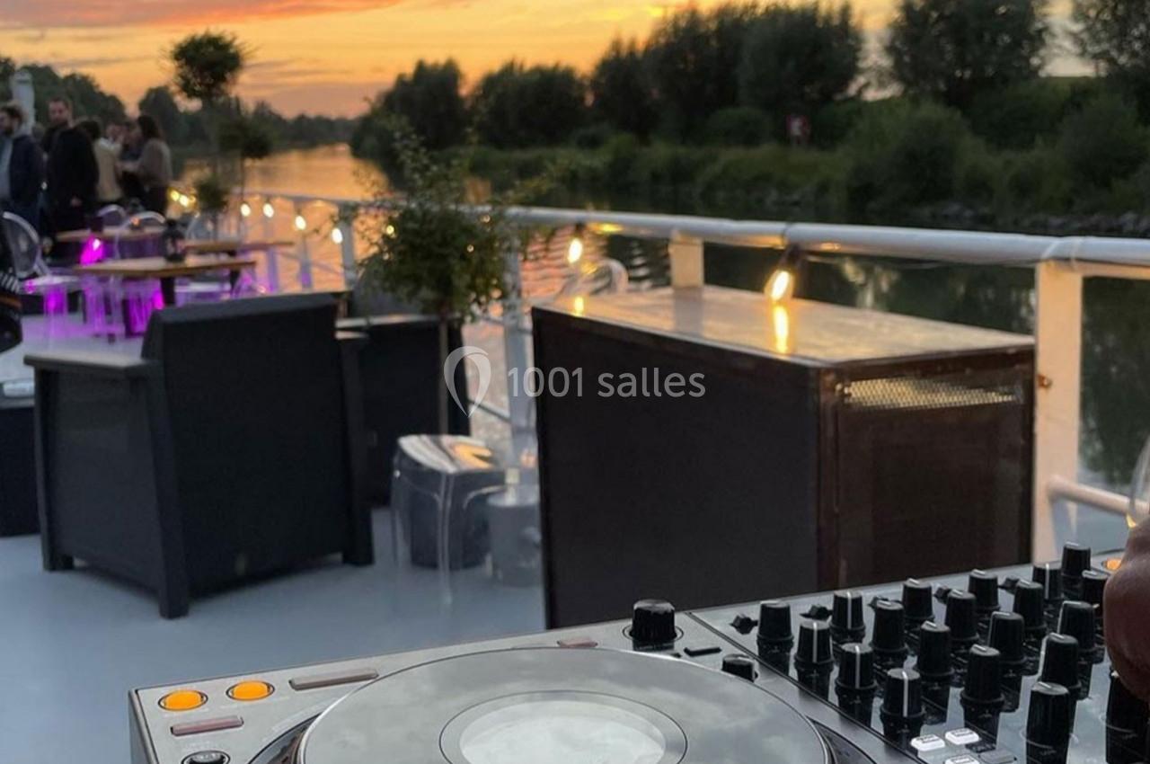 Table de mixage sur le pont d'un bateau au coucher du soleil, avec des invités en arrière-plan près de tables éclairées.