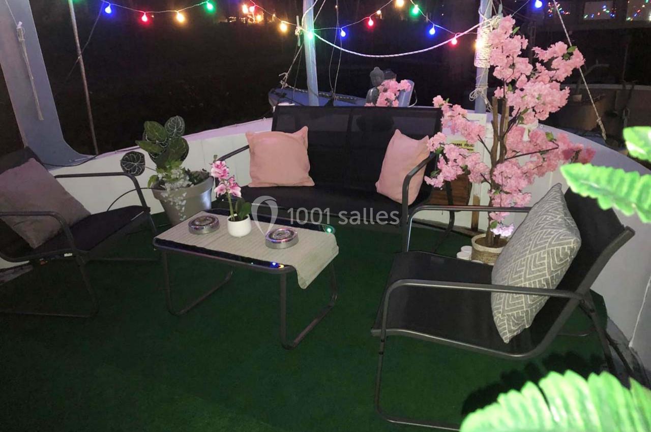 Salon extérieur cosy avec fauteuils, table basse, coussins, plantes décoratives et guirlandes lumineuses colorées.