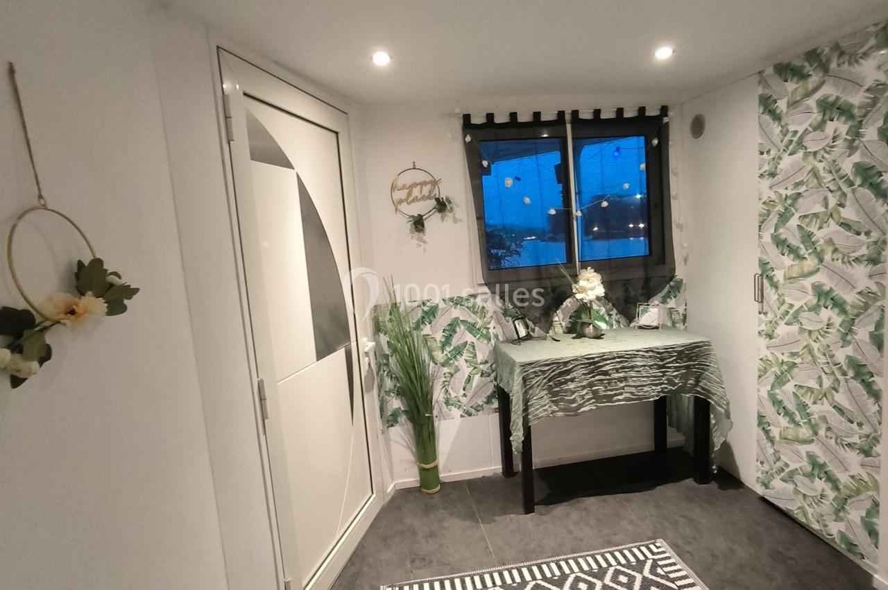 Intérieur lumineux avec décoration végétale, table ornée, tapis à motifs géométriques et fenêtre donnant sur l'extérieur.