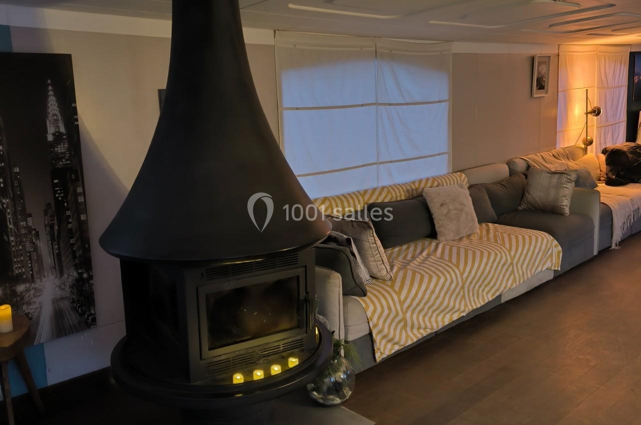 Salon chaleureux avec un poêle noir central, canapé gris et éclairage tamisé dans un intérieur moderne.