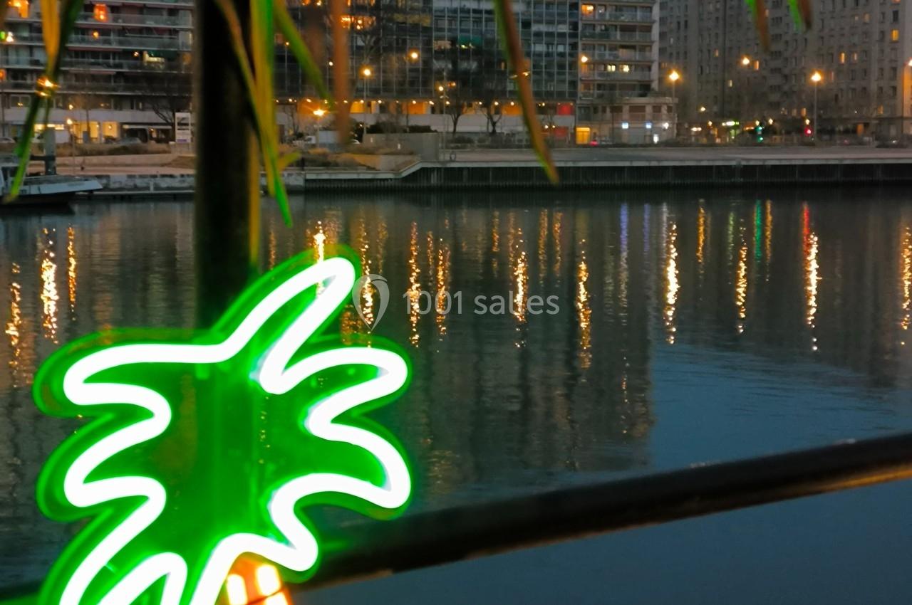 Reflet des lumières urbaines sur l'eau, avec un néon en forme de palmier au premier plan.