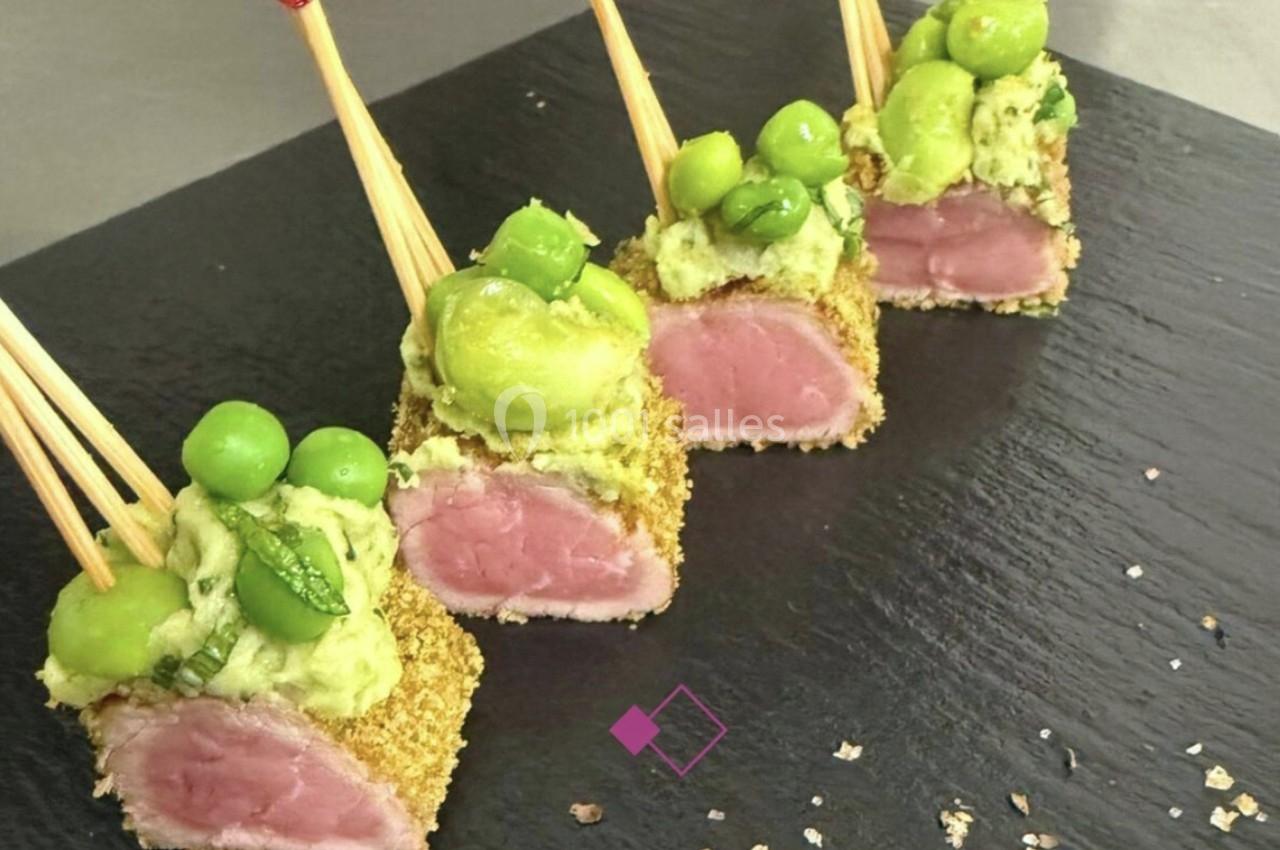 Bouchées de viande panée sur piques, garnies de purée d'avocat et petits pois, présentées sur une ardoise noire.