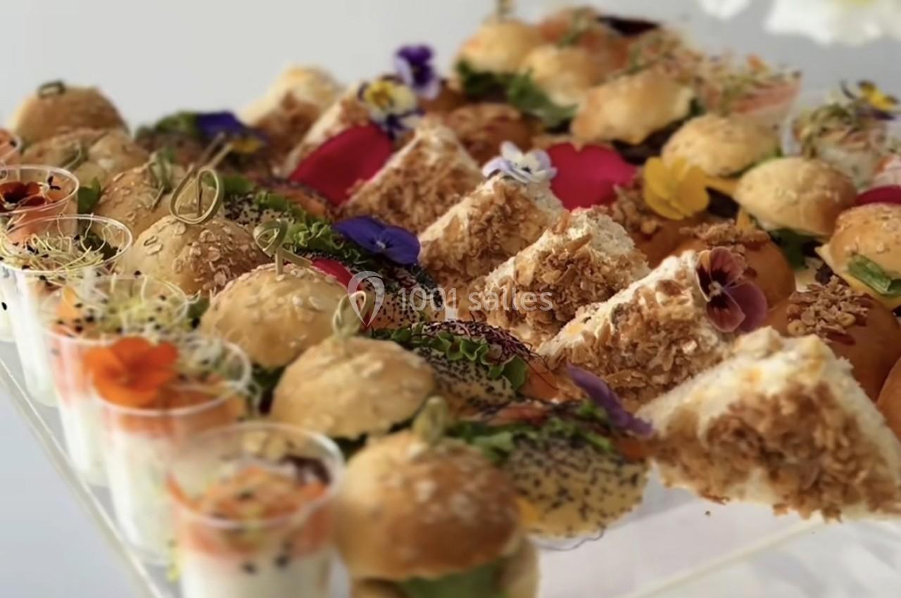 Plateau de mini-sandwichs variés, verrines et décorations florales comestibles, présenté sur une table.