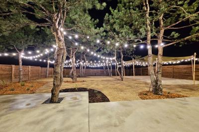 Espace extérieur avec sol en gravier, arbres, tente beige tendue et clôture en bois sous un ciel nuageux.