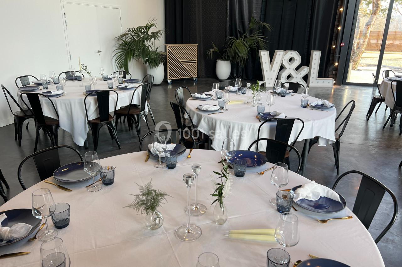 Salle de réception décorée avec des tables rondes dressées, nappes blanches, vaisselle élégante et initiales lumineuses ’V&L…