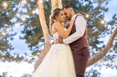 Espace extérieur avec sol en gravier, arbres, tente beige tendue et clôture en bois sous un ciel nuageux.