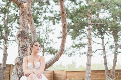 Espace extérieur avec sol en gravier, arbres, tente beige tendue et clôture en bois sous un ciel nuageux.