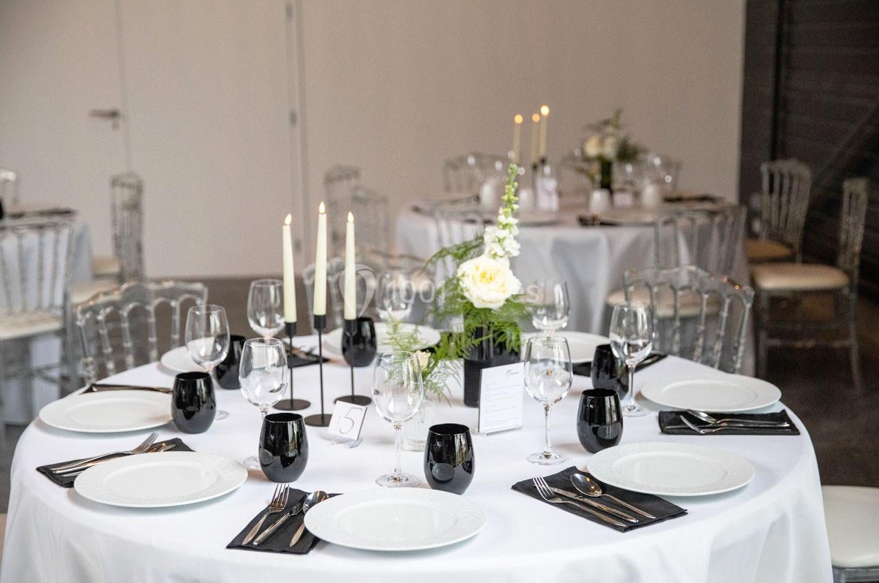 Table dressée avec nappes blanches, vaisselle élégante, bougies allumées et décoration florale au centre.