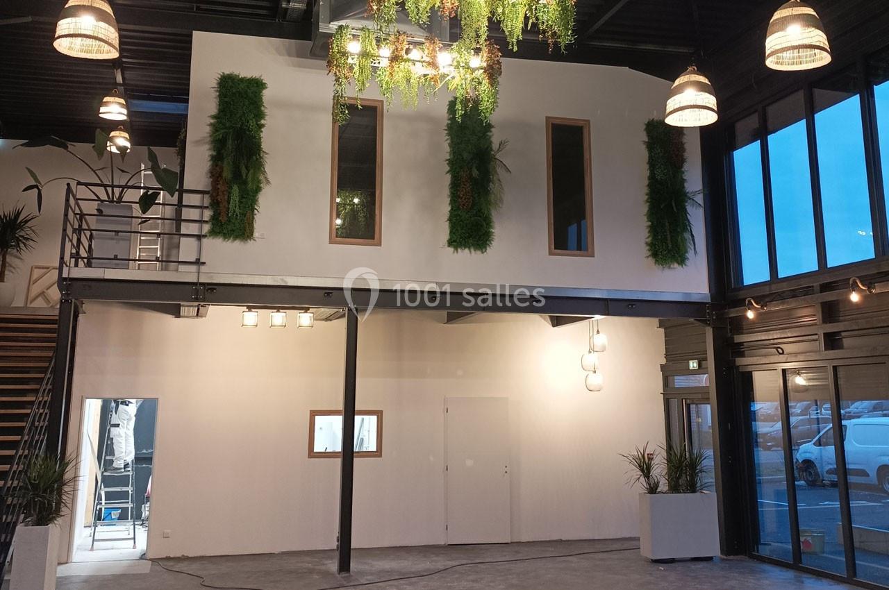 Mezzanine moderne avec murs blancs, fenêtres, plantes suspendues et éclairage industriel dans un espace intérieur spacieux.