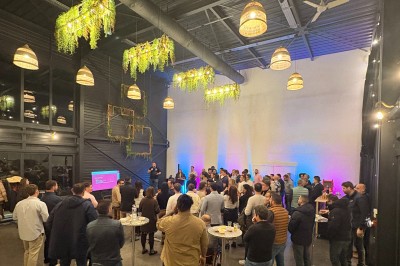 Espace extérieur avec sol en gravier, arbres, tente beige tendue et clôture en bois sous un ciel nuageux.