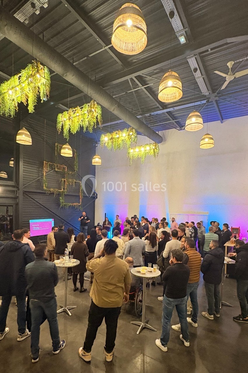 Groupe de personnes rassemblées dans une salle moderne avec des lumières suspendues et des plantes décoratives.