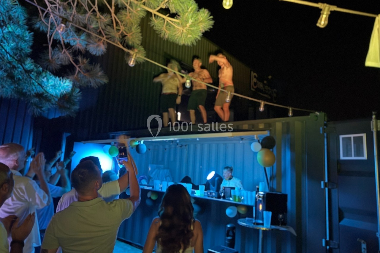 Des personnes dansent sur le toit d'un conteneur éclairé, entouré de spectateurs lors d'une fête nocturne.