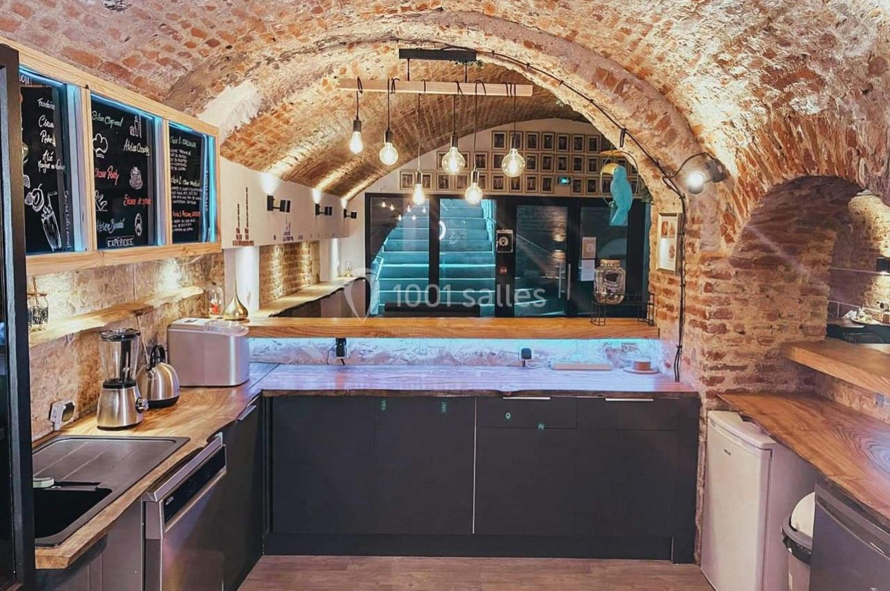 Cuisine moderne sous une voûte en briques avec éclairage suspendu, comptoirs en bois et équipements électroménagers.