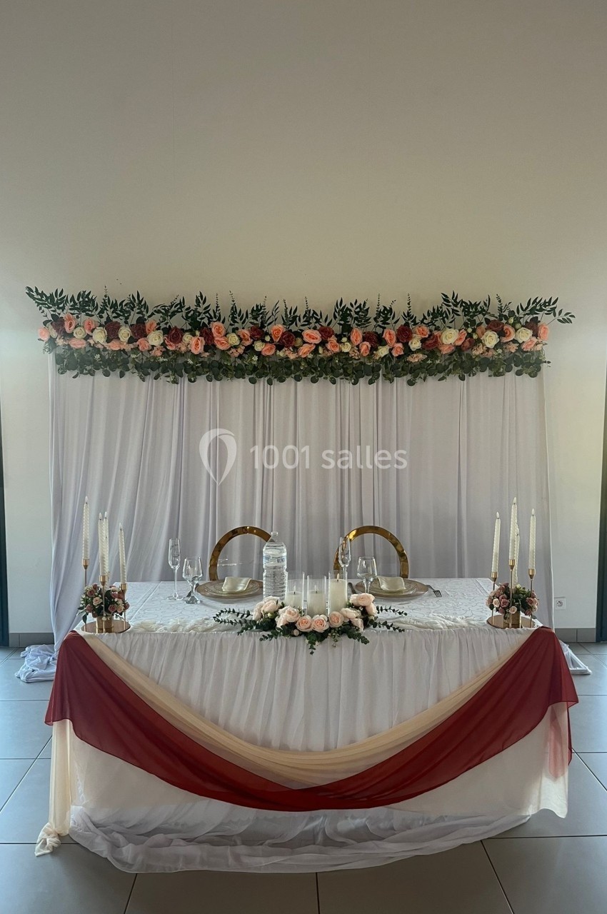 Table décorée pour un mariage avec nappes blanches, drapés bordeaux, chandeliers et guirlande de fleurs en arrière-plan.