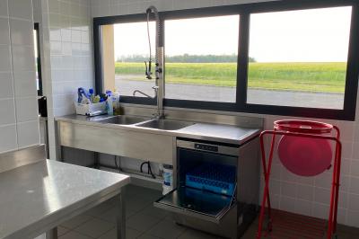 Salle de réception décorée avec des tables dressées, nappes blanches, serviettes rouges et centre de table fleuri.