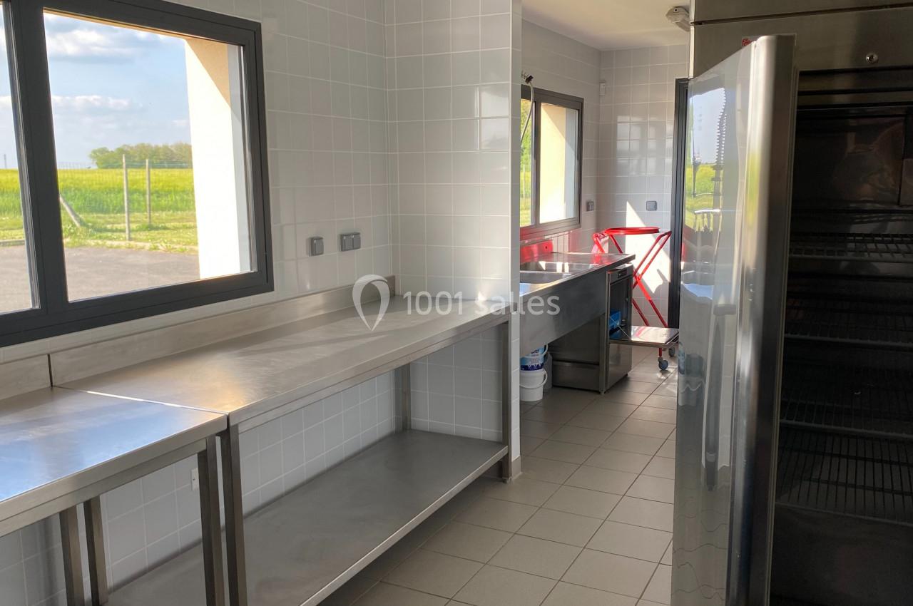 Cuisine professionnelle lumineuse avec plans de travail en inox, carrelage blanc et vue sur un champ à travers les fenêtres.