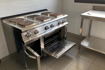 Salle de réception décorée avec des tables dressées, nappes blanches, serviettes rouges et centre de table fleuri.