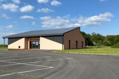 Salle de réception décorée avec des tables dressées, nappes blanches, serviettes rouges et centre de table fleuri.