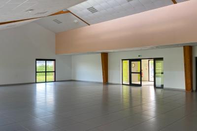 Salle de réception décorée avec des tables dressées, nappes blanches, serviettes rouges et centre de table fleuri.