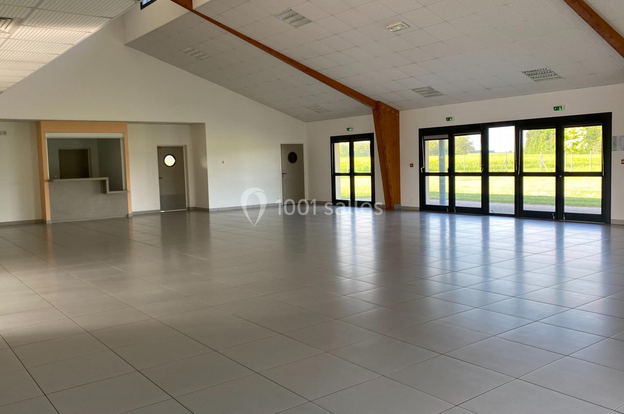 Salle spacieuse avec sol carrelé, grandes baies vitrées, murs blancs et un comptoir à gauche.