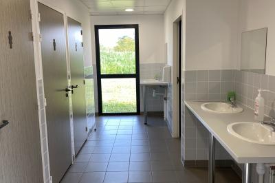 Salle de réception décorée avec des tables dressées, nappes blanches, serviettes rouges et centre de table fleuri.