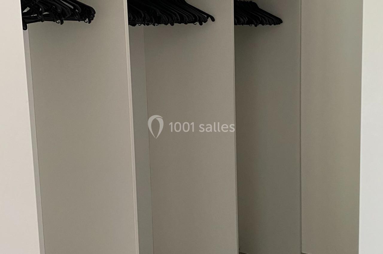 Placard ouvert avec trois compartiments équipés de tringles et de cintres noirs, sol carrelé et murs blancs.