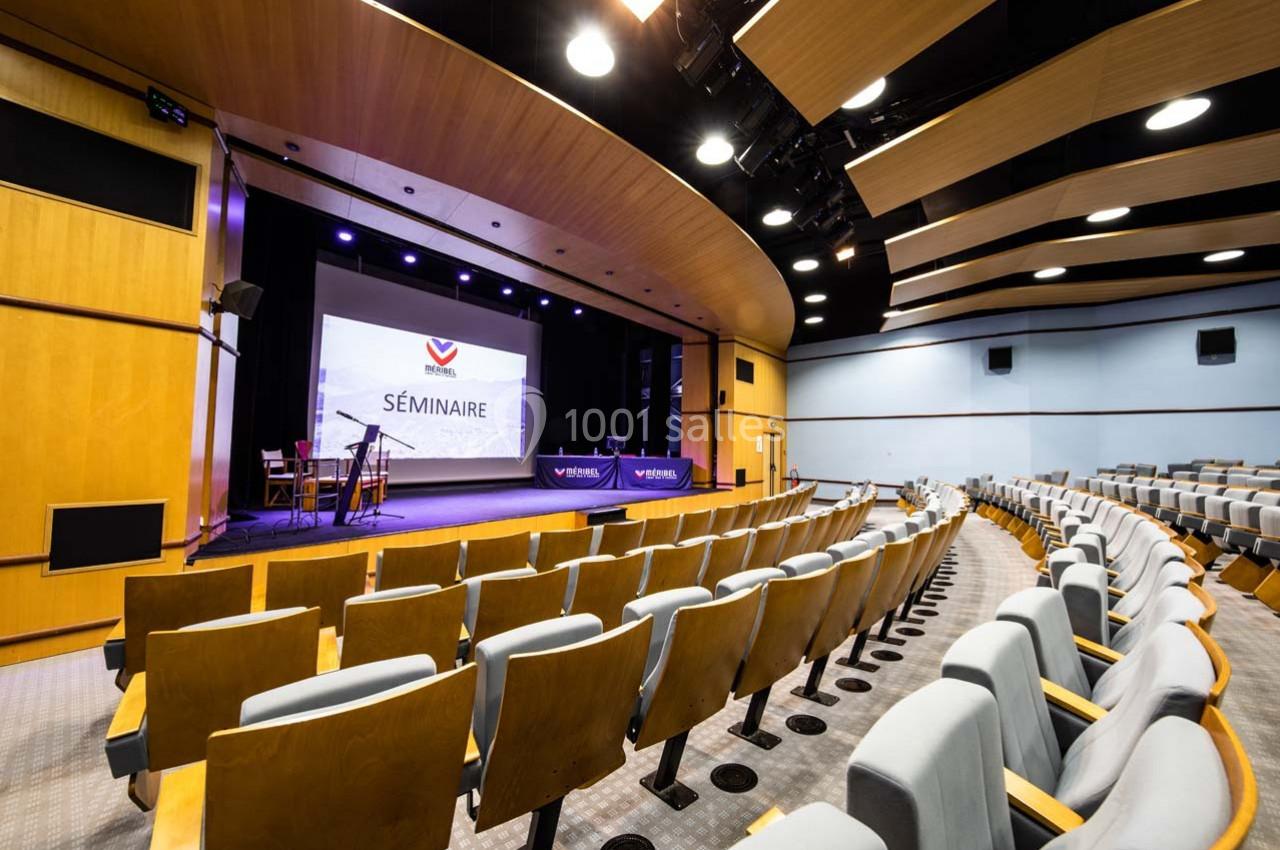 Salle de conférence moderne avec sièges alignés, scène équipée et écran affichant ’Séminaire’.