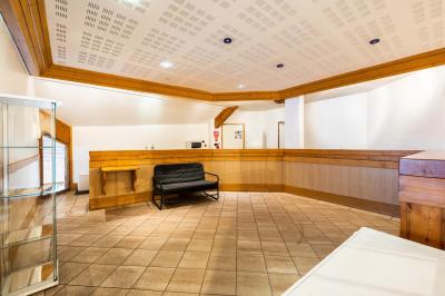 Entrée lumineuse avec tapis foncé, murs blancs, escalier en bois et plantes visibles à travers une cloison vitrée.