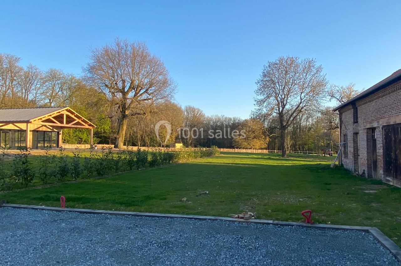 Jardin avec pelouse, gravier au premier plan, bâtiments en briques et structure en bois sous un ciel dégagé.