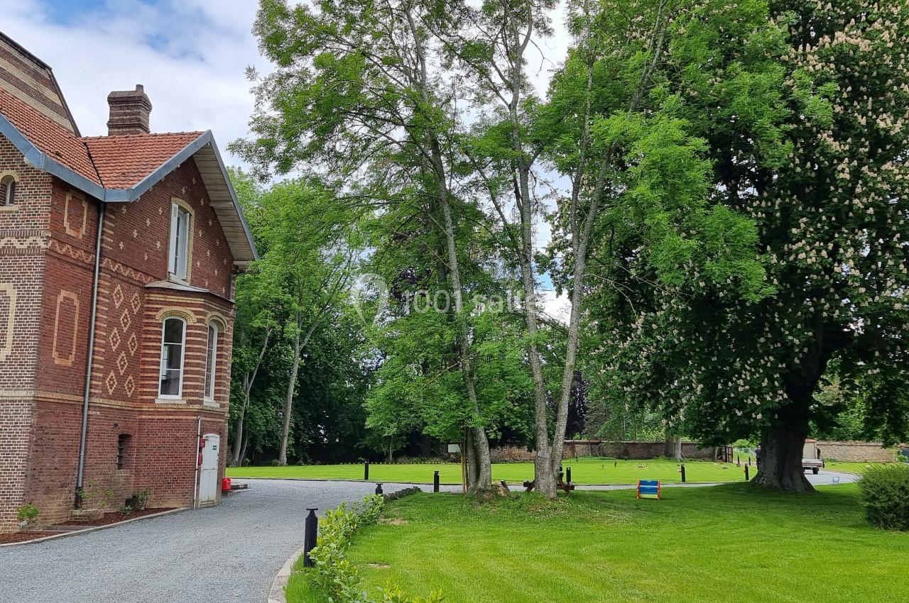 Bâtiment en briques rouges à gauche, entouré d'arbres et d'une pelouse verdoyante sous un ciel partiellement nuageux.